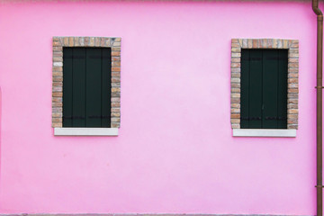 The violet colored bright facade of the building with two windows covered with wooden shutters. Bright wall of residential building in Italian architecture style. The space on the wall for inscription