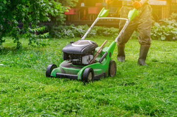 Green gasoline lawn mower on the grass in the park on the lawn