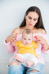 happy mom sits on the floor with her little son on a gray background