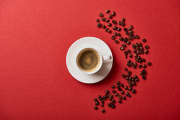 top view of delicious coffee in cup near roasted beans on red background