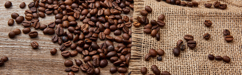 panoramic shot of fresh roasted coffee beans on wooden weather board with sackcloth
