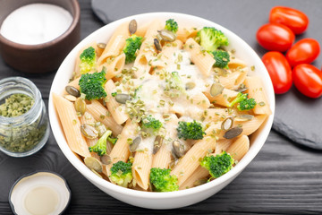 Fototapeta na wymiar Bowl with pasta, green onions, white sauce, pumpkin seeds and broccoli. On the table are cherry tomatoes, salt, green onions. 