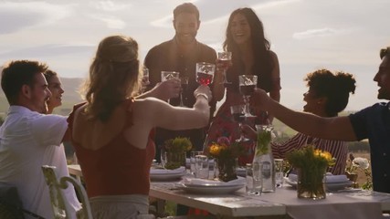Group of friends toasting wine at dinner party outdoors. Young people enjoying having drinks at dinner at backyard garden. - Powered by Adobe