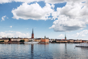 Fototapeta na wymiar Scenic summer panorama of the Old Town (Gamla Stan) architecture in Stockholm, Sweden. view from Monteliusvagen hill on island Riddarholm and tower of church. Lake Malaren with blue sky, white clouds.