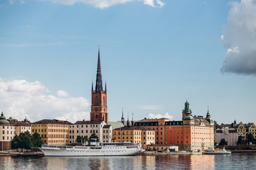 Fototapeta premium Scenic summer panorama of the Old Town (Gamla Stan) architecture in Stockholm, Sweden. view from Monteliusvagen hill on island Riddarholm and tower of church. Lake Malaren with blue sky, white clouds.