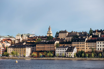 Fototapeta premium Scenic summer panorama of the Old Town (Gamla Stan) architecture in Stockholm, Sweden. view from Monteliusvagen hill on island Riddarholm and tower of church. Lake Malaren with blue sky, white clouds.