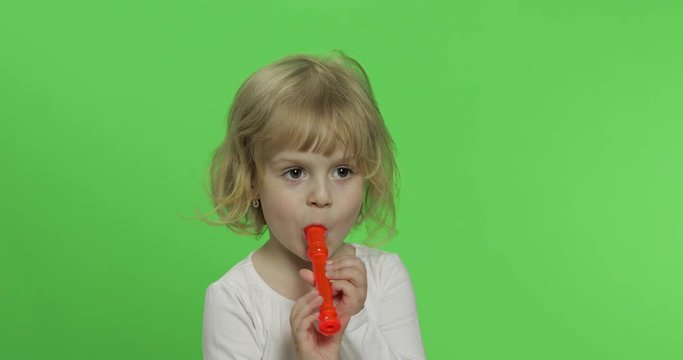 Portrait of three years old blonde girl plays on toy pipe on green background