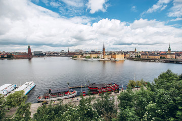 Naklejka premium Scenic summer panorama of the Old Town (Gamla Stan) architecture in Stockholm, Sweden. view from Monteliusvagen hill on island Riddarholm and tower of church. Lake Malaren with blue sky, white clouds.