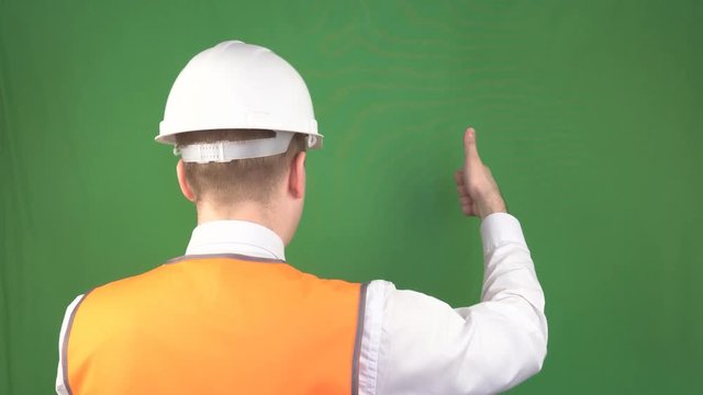 Male builder in a protective helmet and signal vest shows commands with gestures at a construction site, safety engineering, industry, hromakey