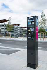 A parking meter in town in front of a modern building