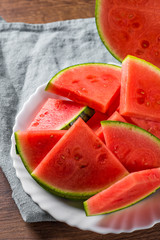 Cut slices of juicy watermelon on white plate on wooden table background