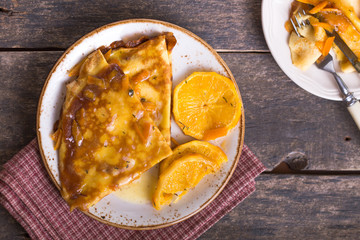 Pancakes crepe Suzette for breakfast with orange caramel sauce, orange slices, lime and orange zest and a cup of coffee. Dessert French cuisine. Sunday breakfast