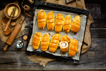 Overhead shot of delicious homemade baked sausages rolled in dough on baking tray on wooden rustic table