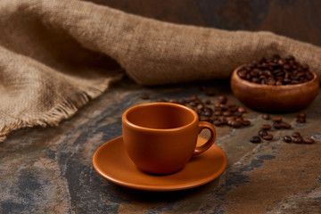 brown cup on saucer on marble surface near sackcloth and coffee beans