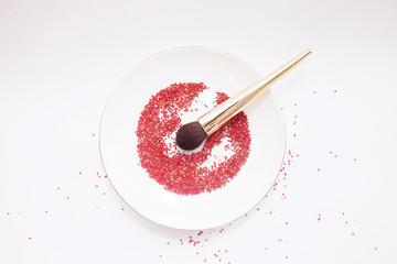 beauty concept and art. A brush for powder with a gold handle lies on a white plate in a red pastry dressing. top view