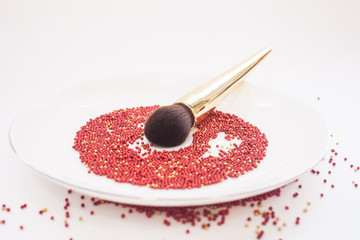 beauty concept and art. A brush for powder with a gold handle lies on a white plate in a red pastry dressing