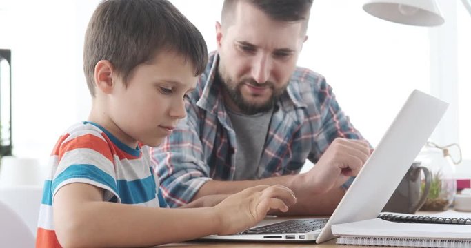 Father guiding his son learning to operate laptop computer at home