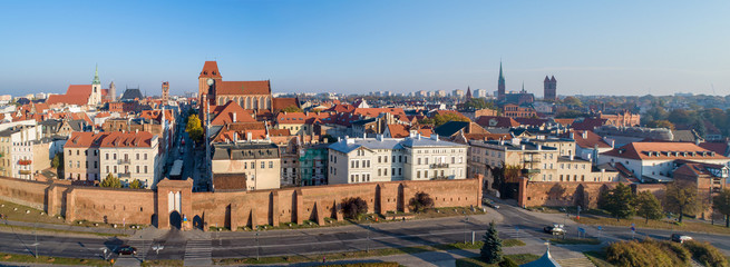 Wide aerial panorama of Torun Old City in Poland with Medieval Gothic Cathedral of St. John, town hall clock tower, churches, defensive wall and city gates. Skyline in sunrise light