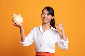 Asian woman thumbs up with pig coin bank.