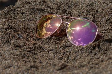 Sunglasses at the beach with sky and sun reflection. Holidays, travel, vacation and happiness concept.