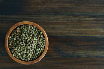 Dried green peppercorns in a wooden bowl. Dark wooden table, high resolution, negative space