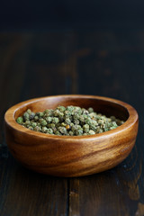 Dried green peppercorns in a wooden bowl. Dark wooden table, high resolution