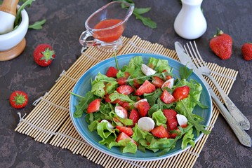 Salad with strawberries, arugula and mozzarella cheese on a dark brown background concrete. Healthy food.