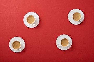 top view of white cups with delicious coffee on saucers on red background