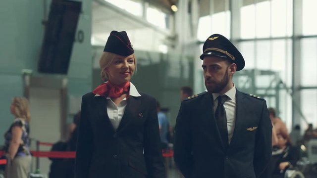 Handsome male pilot and attractive female flight attendant are walking in airport terminal together.