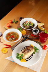 Diet, but nutritious lunch in a restaurant, served on a wooden table: pork patty with boiled bulgur, hot soup with meatballs and vegan pasta with olives  as a nutritious lunch in a cafe