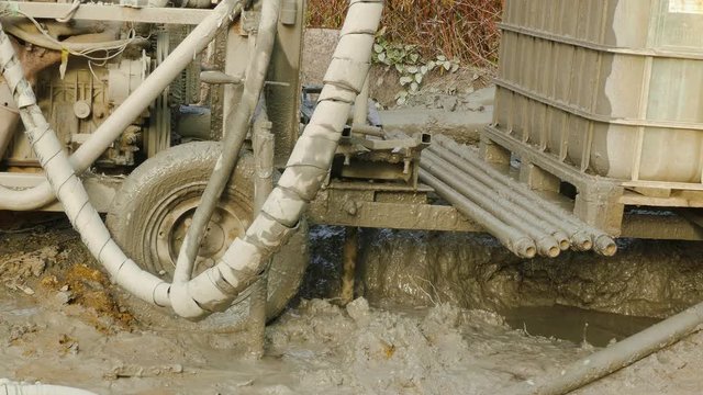 Dirty machine lifts drill up from dirt to create a well