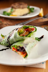 Yummy vegan spring rolls in a rice paper with carrot, greens, bell pepper and cucumber on a dark background