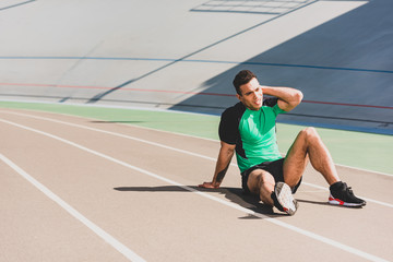 tired bi-racial sportsman in sportswear sitting at stadium