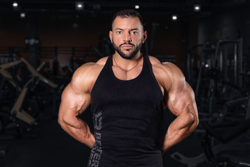 Fototapeta na wymiar Bodybuilder in the gym. Sports photo shoot. Man's fitness. Training and exercises with dumbbells. Men's photo shoot in low key. Athletic build. young man lifting weights in gym 