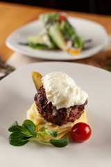 Close up of a meat cutlet, placed on a lay of fluffy mashed potatoes and served with white sauce and veggies