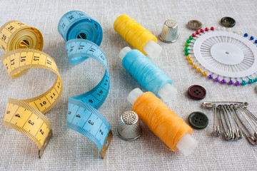 Fototapeta na wymiar sewing tools: colored sewing threads, centimeter ribbons, thimbles, colored pins and a few small buttons on a light gray background close-up