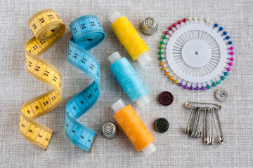 sewing tools: colored sewing threads, centimeter ribbons, thimbles, colored pins and a few small buttons on a light gray background close-up