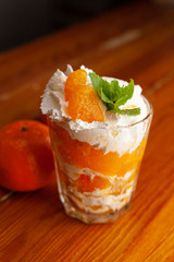 Layered tangerine dessert in a glass with whipped cream cheese, decorated with fresh mint on a wooden background
