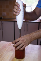  red ripe strawberry smoothie in a glass; male hand is holding a blender