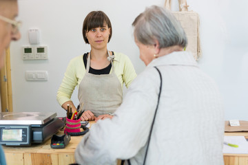 Fototapeta premium Young shopkeeper interacting with elderly lady at cash desk.