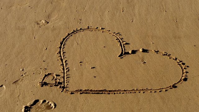 Girl writes a heart symbol in the sand on a beach - travel photography