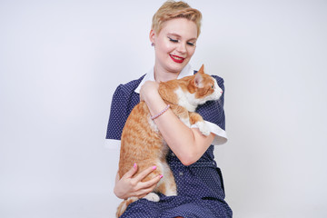 cute kind woman with short hair in pinup polka dot dress holding her beloved pet on a white background in the Studio. plus size adult blonde girl and her orange cat are happy together.