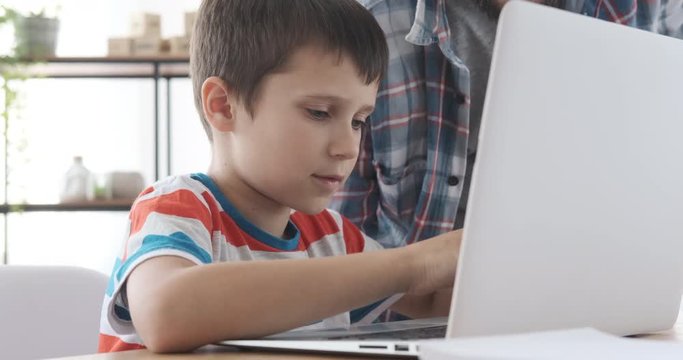 Young father and son talking while using laptop at home