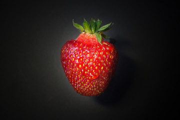 Fresh strawberries in a bowl on wooden table with low key scene.