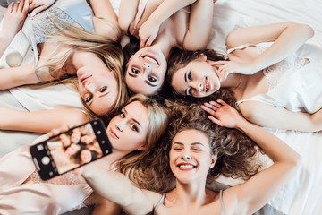 Photo of sexy,  cheerful girls in night wear lying on bed, making selfie, looking  and posing at camera.. Hen party.