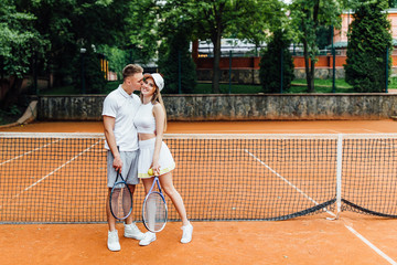 Tennis time, couple relaxing after playing game of tennis outside in summer. Hugging couple.