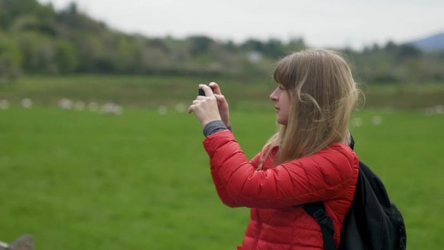 Young woman takes photos of the typical green landscape in Ireland - travel photography