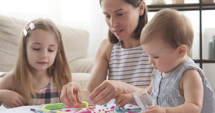 Mother and two little girls having fun playing with plasticine at home