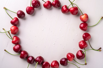 Copy space circle of cherry berries with stem on wooden white background and water drops top view