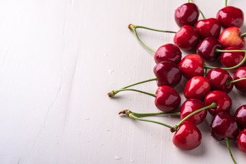Cherry berries with stem on wooden white background and water drops